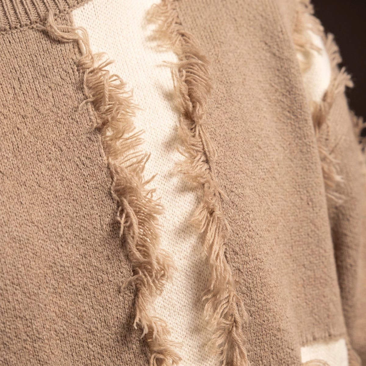 Verrick Distressed Sweater close up of a torn knit band, loose frayed yarn and the smooth contrast layer behind it