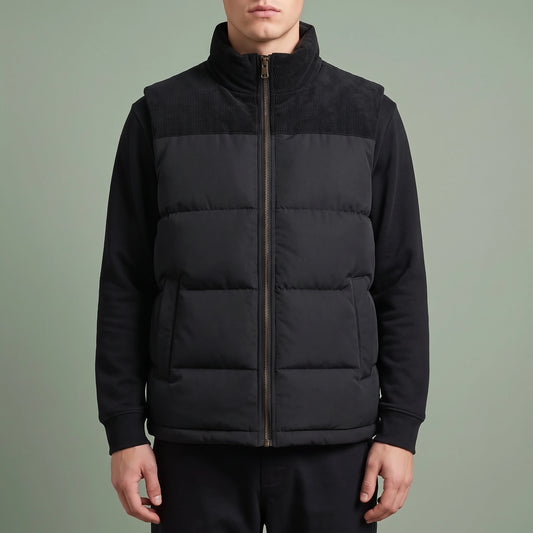 Brancourt Puffer Vest in Black - quilted sleeveless vest with corduroy stand collar and shoulder yokes, worn over a long-sleeve top by a model in studio