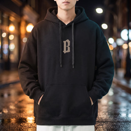 Vallor Gothic Hoodie in black, oversized pullover with small blackletter B chest print, worn on a city street at night